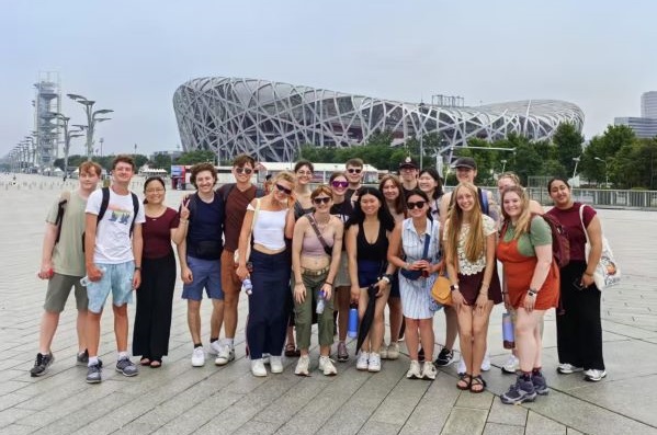 Students stand in front of the National Stadium, also known as the Bird's Nest